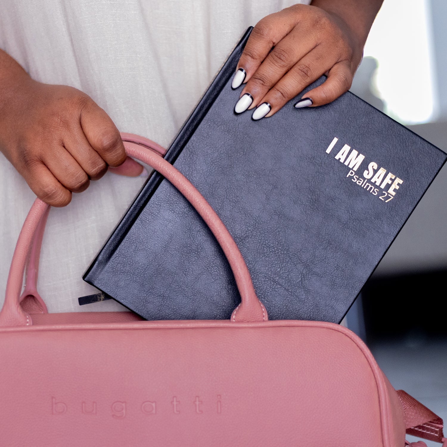 Person holding a pink handbag with a blue book titled 'I AM SAFE Psalms 27' on a blurred background