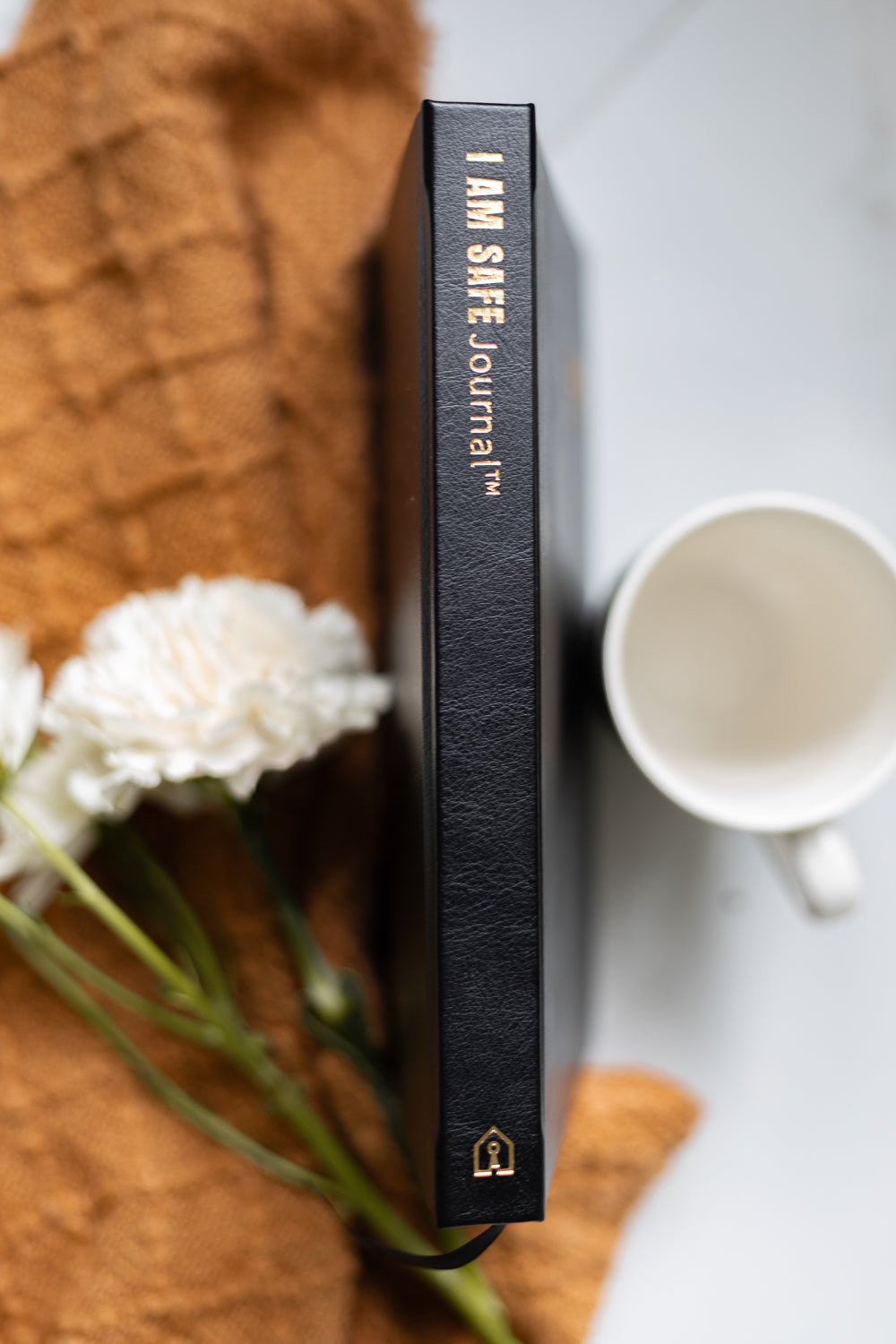 Black journal titled 'I AM SAFE Journal' on a surface with flowers and a mug.