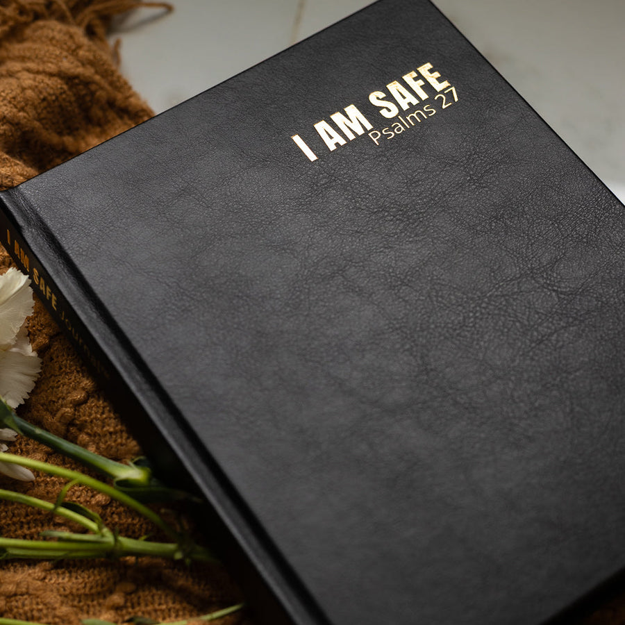 Woman sitting on a couch with a book titled 'I AM SAFE' in front of her.