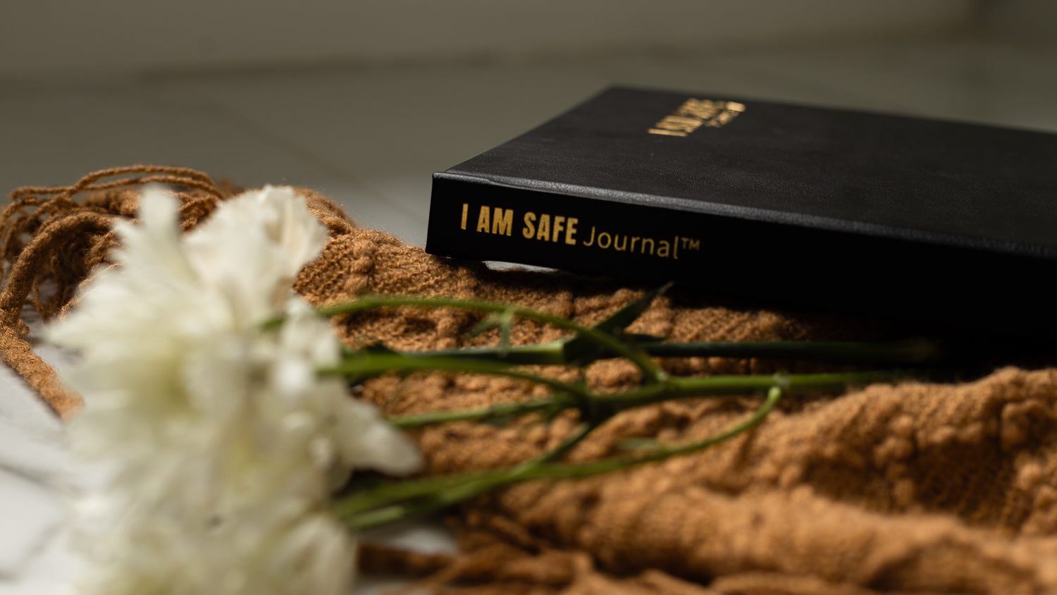 Black 'I AM SAFE Journal' on a textured surface with white flowers