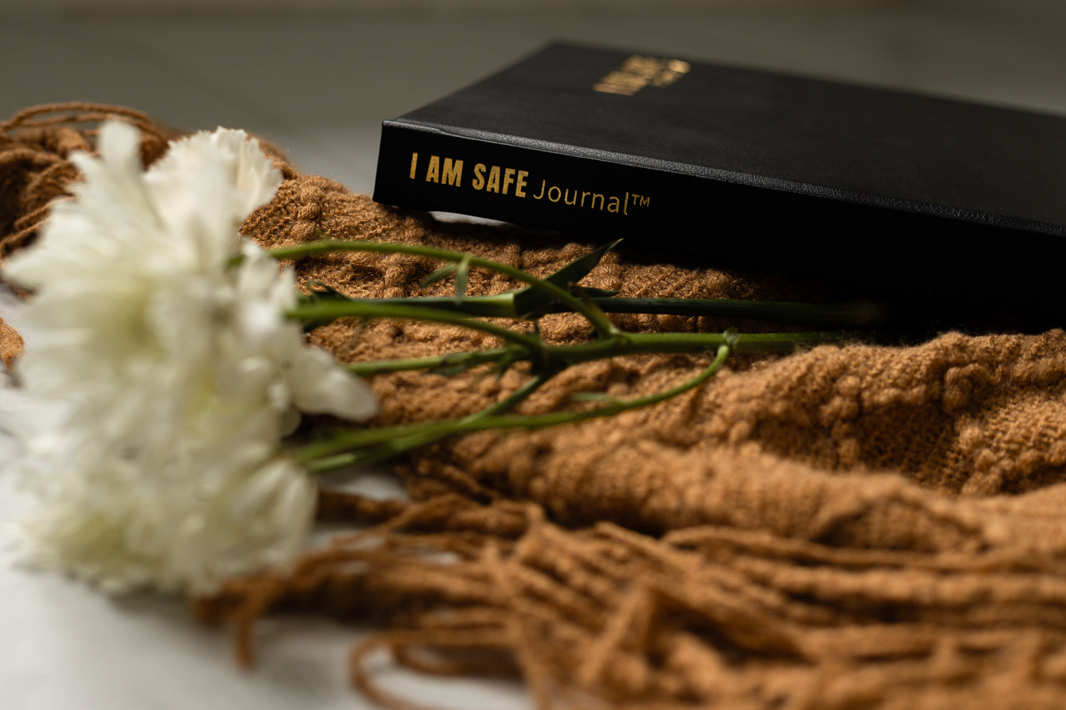 Black 'I AM SAFE Journal' on a textured surface with white flowers