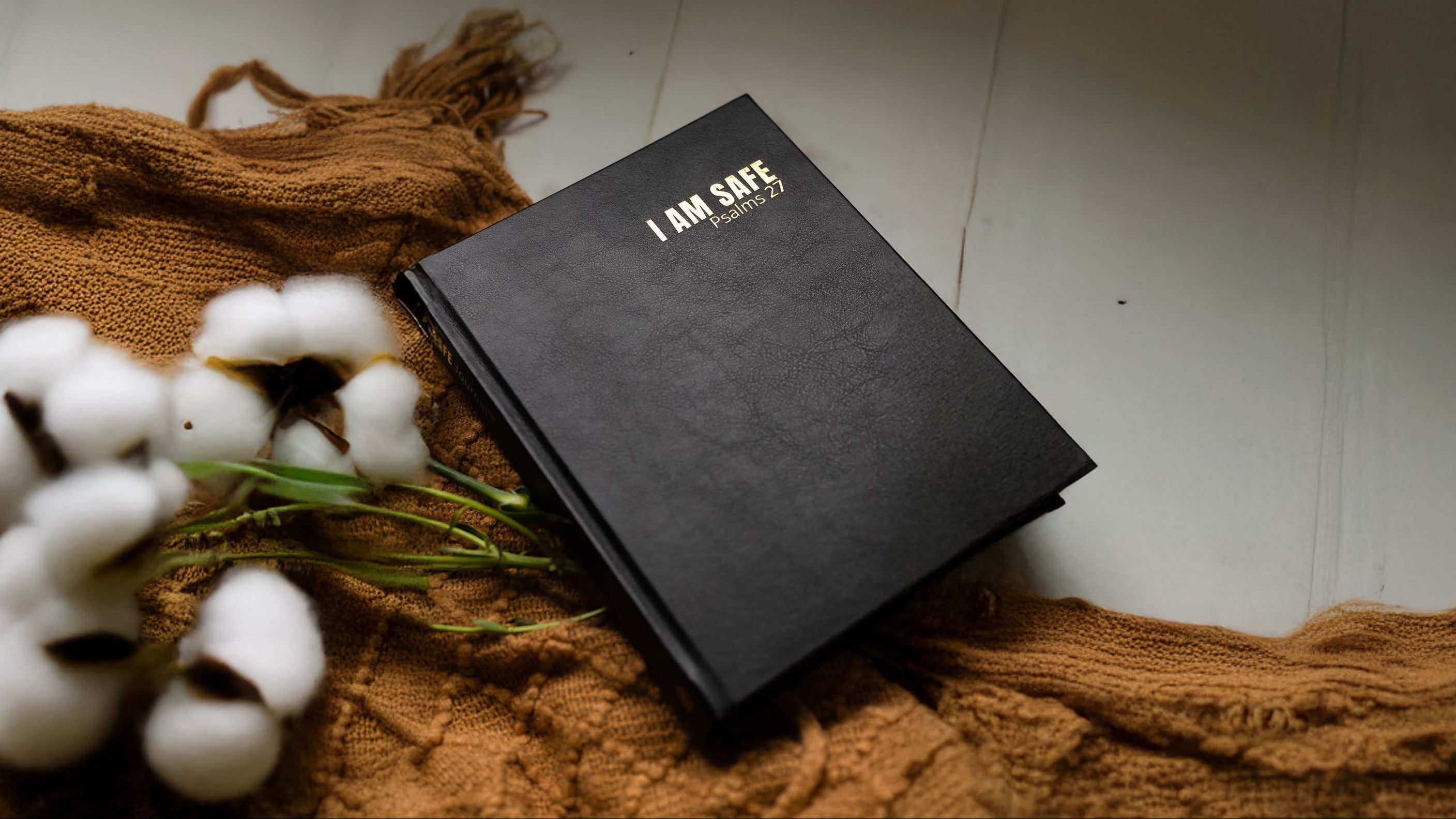 Black notebook titled 'I AM SAFE' on a textured surface with cotton flowers