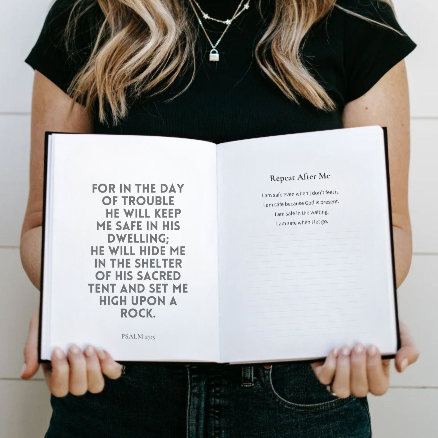 Person holding an open book with text, wearing a black shirt and necklace.