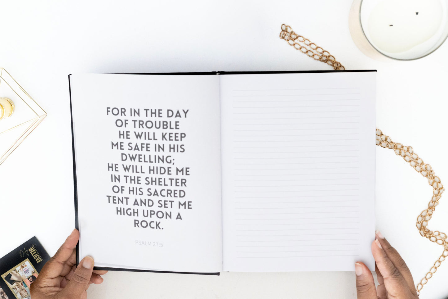 Open IAN SAFE Journal with a biblical verse, held by hands on a white surface with a candle and chain.