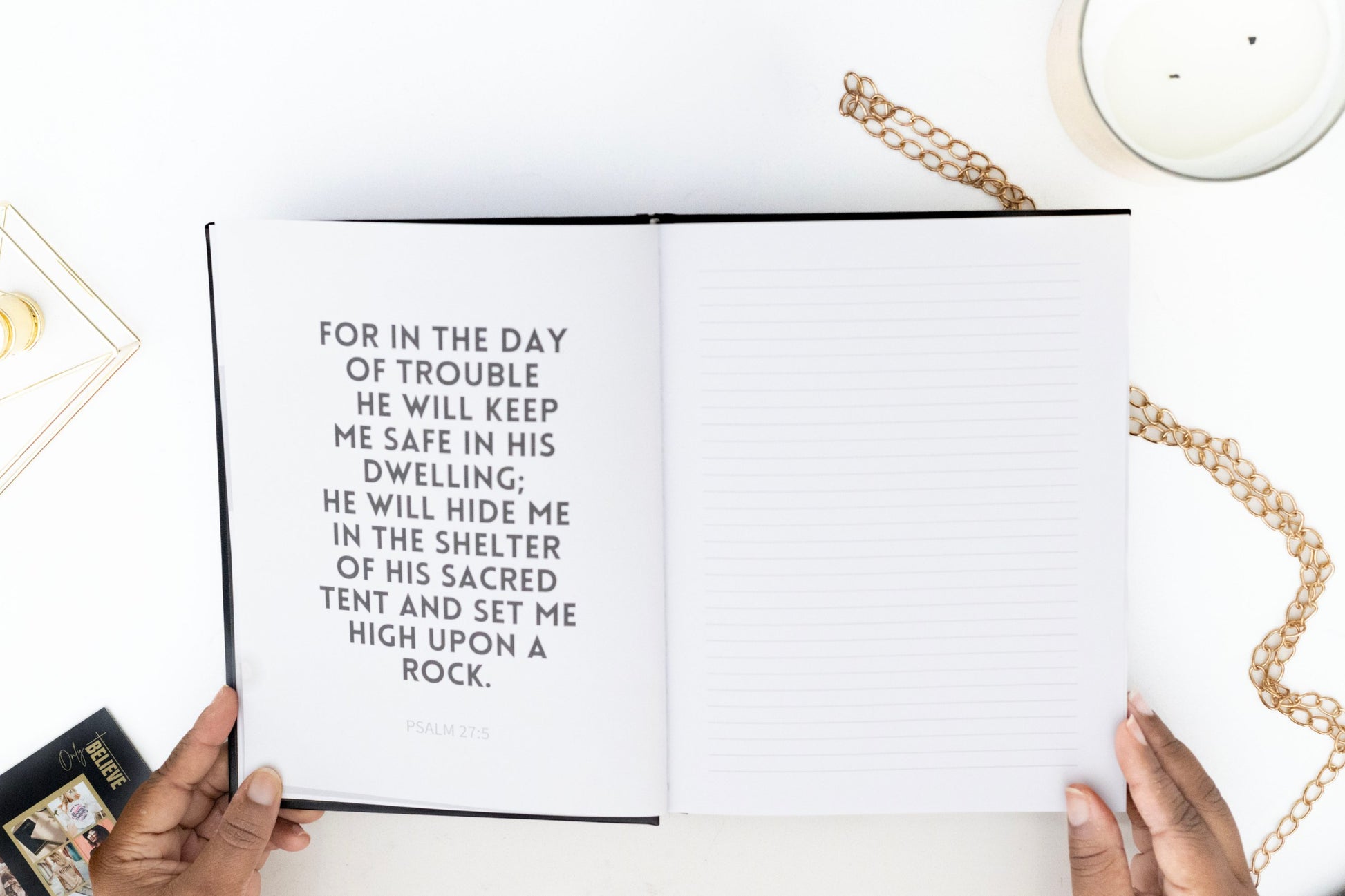 Open IAN SAFE Journal with a biblical verse, held by hands on a white surface with a candle and chain.
