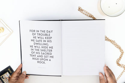 Open IAN SAFE Journal with a biblical verse, held by hands on a white surface with a candle and chain.