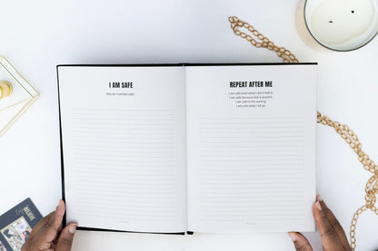 Open I AM SAFE Journal with affirmation text on a white surface with hands holding it