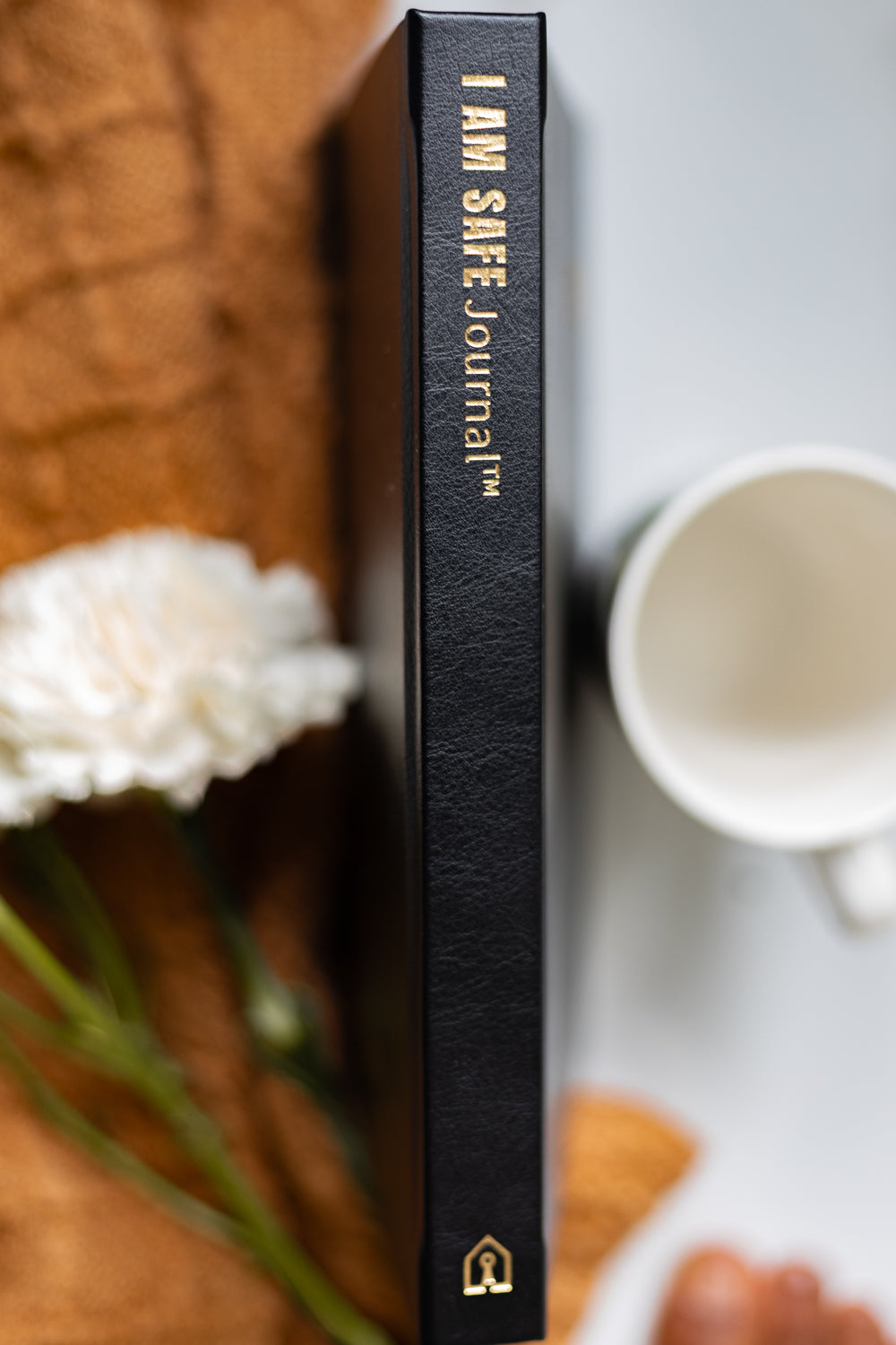 Black journal titled 'I AM SAFE'  with a blurred background of a cup and flowers.