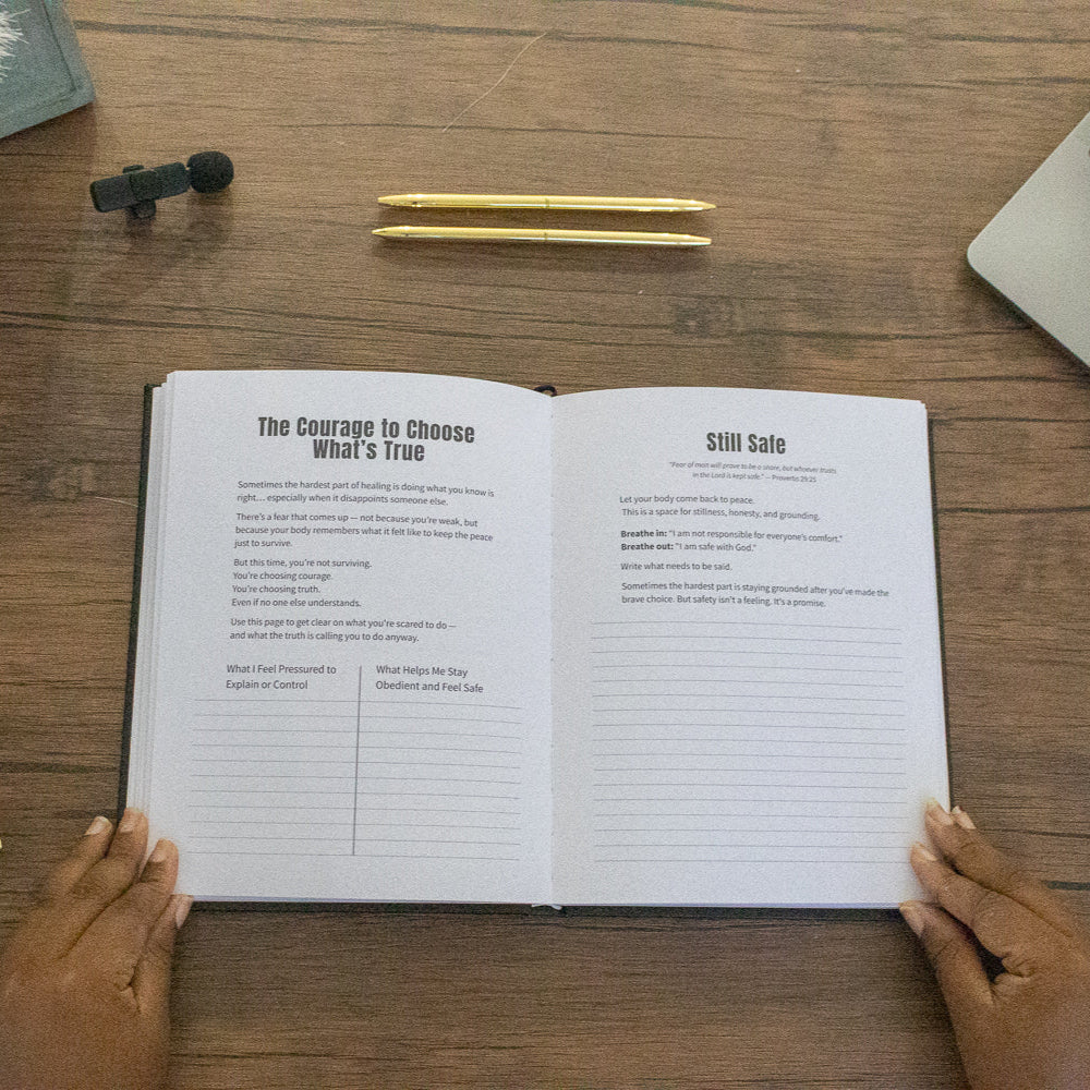 Open book on a wooden desk with a laptop, pen, and decorative items.