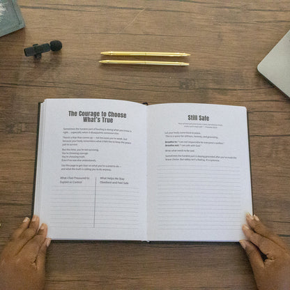 Open book on a wooden desk with a laptop, pen, and decorative items.