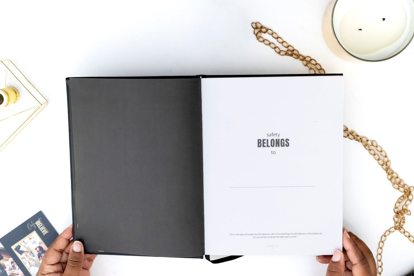 Open I AM SAFE Journal with a page titled 'Safety Belongs to Me' on a white surface with gold chains and a candle.
