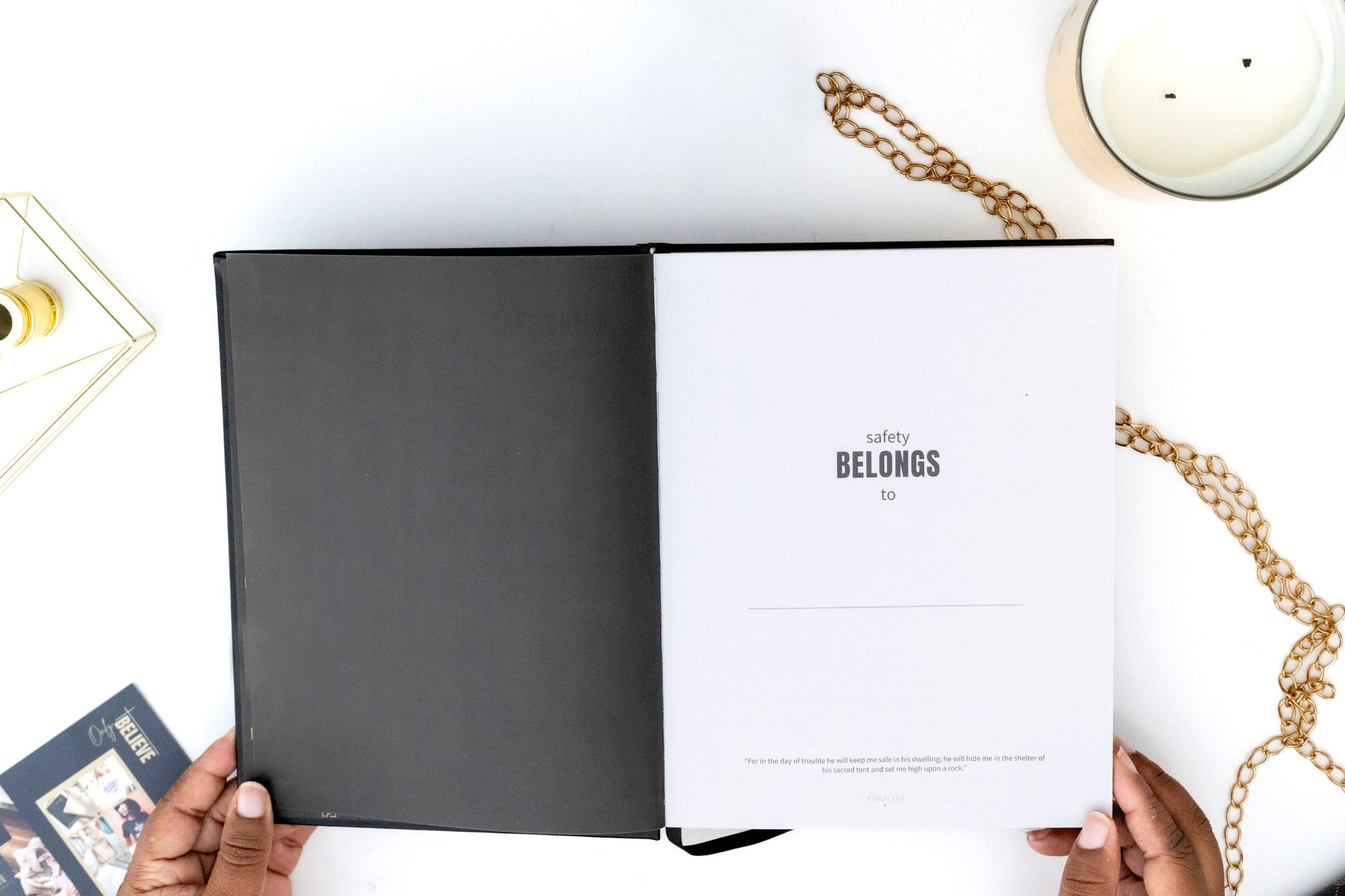 Open I AM SAFE Journal with a page titled 'Safety Belongs to Me' on a white surface with gold chains and a candle.